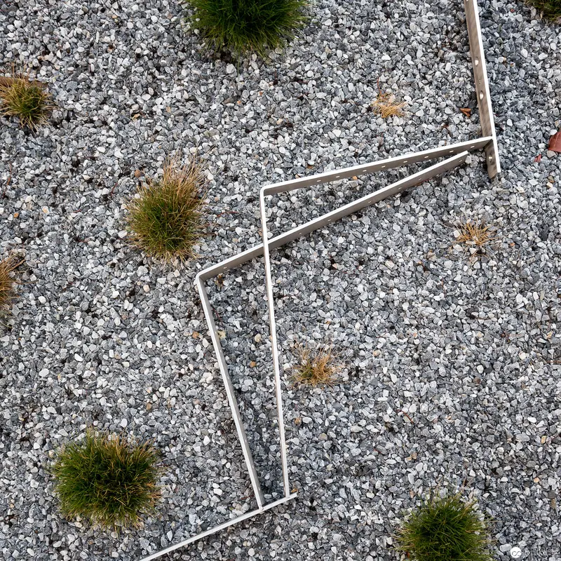 Geometric Metal Framework Amidst Gray Gravel and Sparse Green Vegetation Clusters