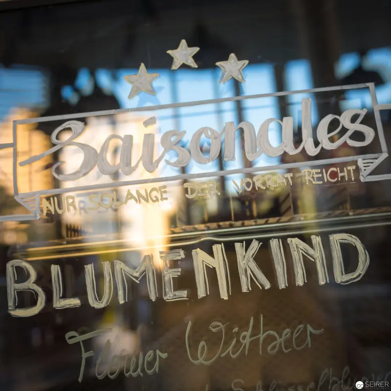 Saison Sales Window Display with Blumenkind Signage in Reflective Urban Setting