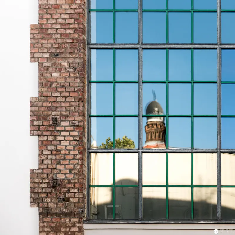 Architectural Reflection: Brick Wall Intersecting Modern Glass Facade with Historic Dome