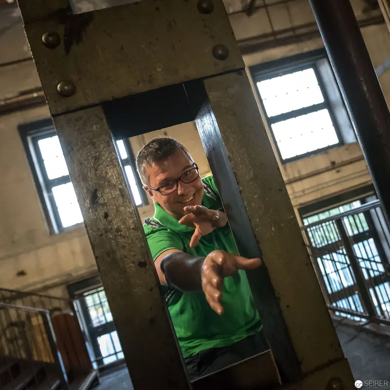 Confined Figure in Green Shirt Gesturing Through Industrial Metal Framework