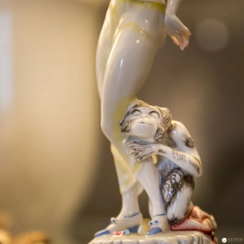 Porcelain Figurine of Playful Monkey Positioned Beneath Delicate Statuesque Limb