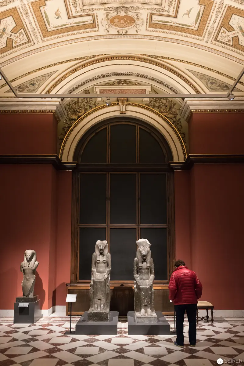 Ancient Egyptian Statues in Ornate Museum Gallery with Visitor
