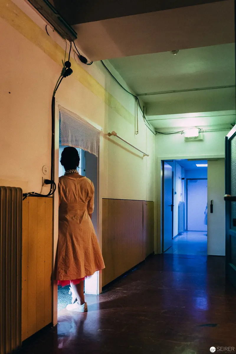 Performer in Orange Coat Illuminated in Blue-Tinted Hallway during "Dirty Faust" Performance