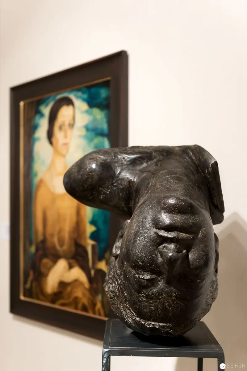 Dark Sculptural Head Contrasts with Colorful Portrait at Art Exhibition
