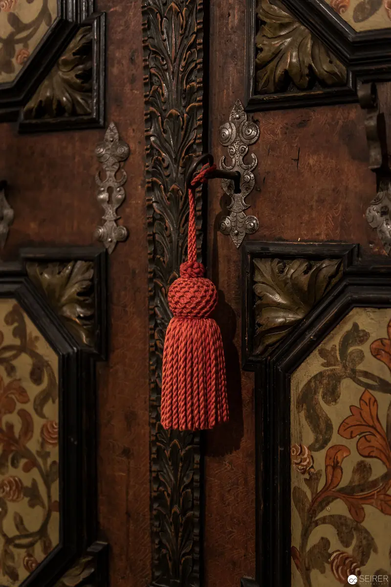 Crimson Tassel on Ornate Wooden Panel with Baroque Decorative Detailing