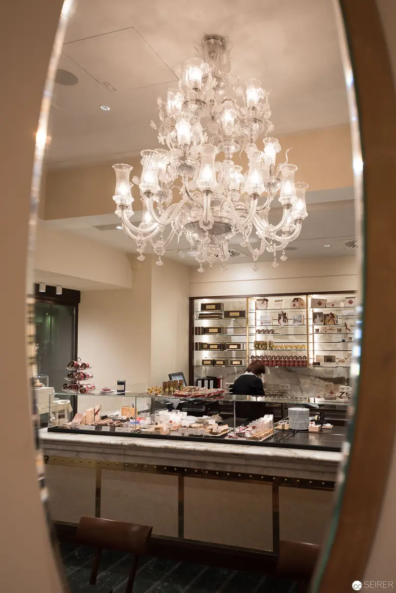 Crystal Chandelier Illuminating Elegant Pastry Kitchen Through Framed Reflection