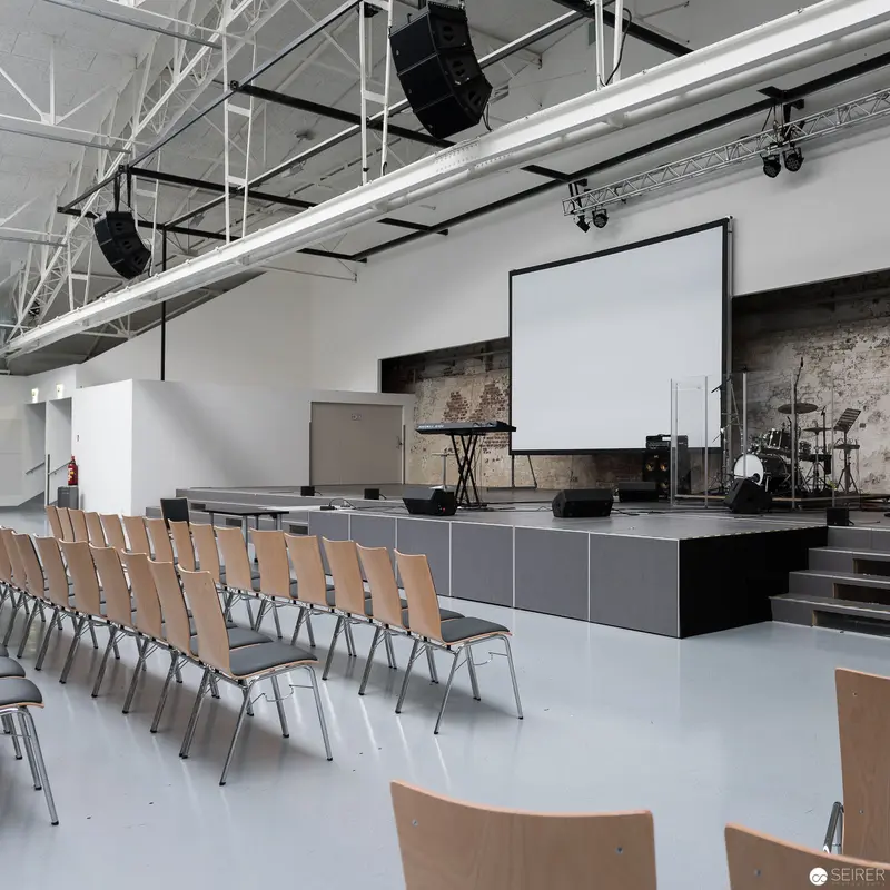 Minimalist Event Space with Projection Screen and Staged Performance Area, Expedithalle Anker Brotfabrik