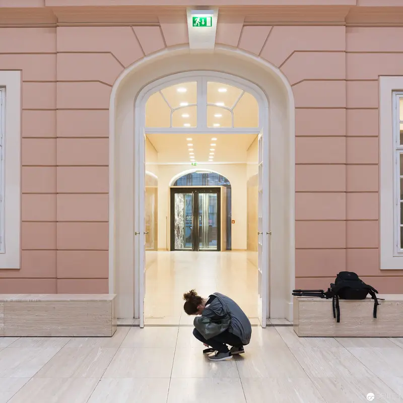 Solitary Figure Crouched in Institutional Archway During Museum Exhibition Installation