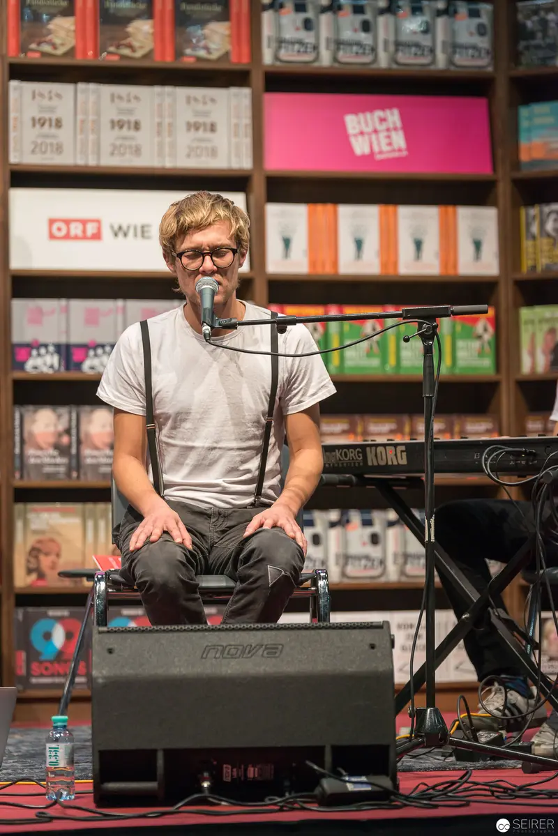 Performer at Book Event Seated with Microphone Amid Publication Displays