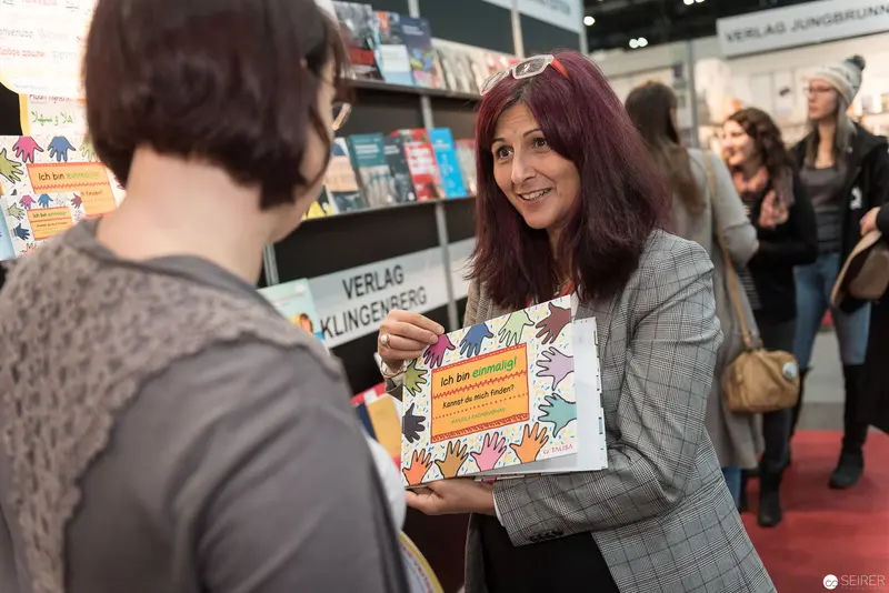 Book Wien 2017: Publisher Representative Displaying Colorful Illustrated Book at Literary Fair