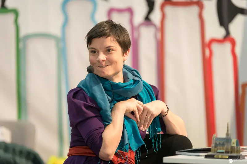 Lena Raubaum in Teal Scarf, Framed by Colorful Silhouettes