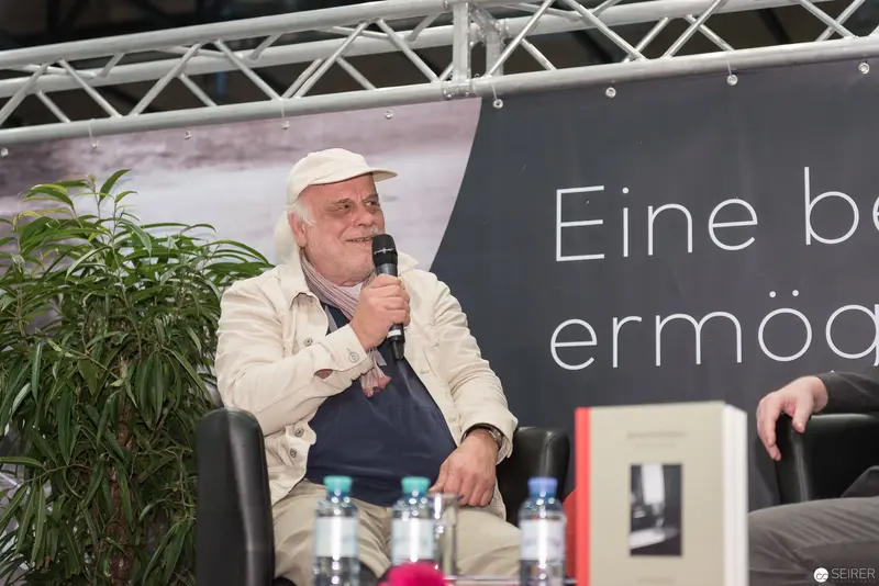 Reflective Author at Book Event in Vienna, Speaking with Microphone