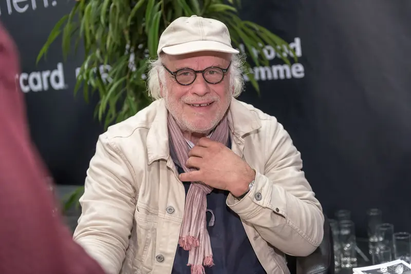 Smiling Author at Literary Event in Vienna, Wearing Cream Jacket and Cap