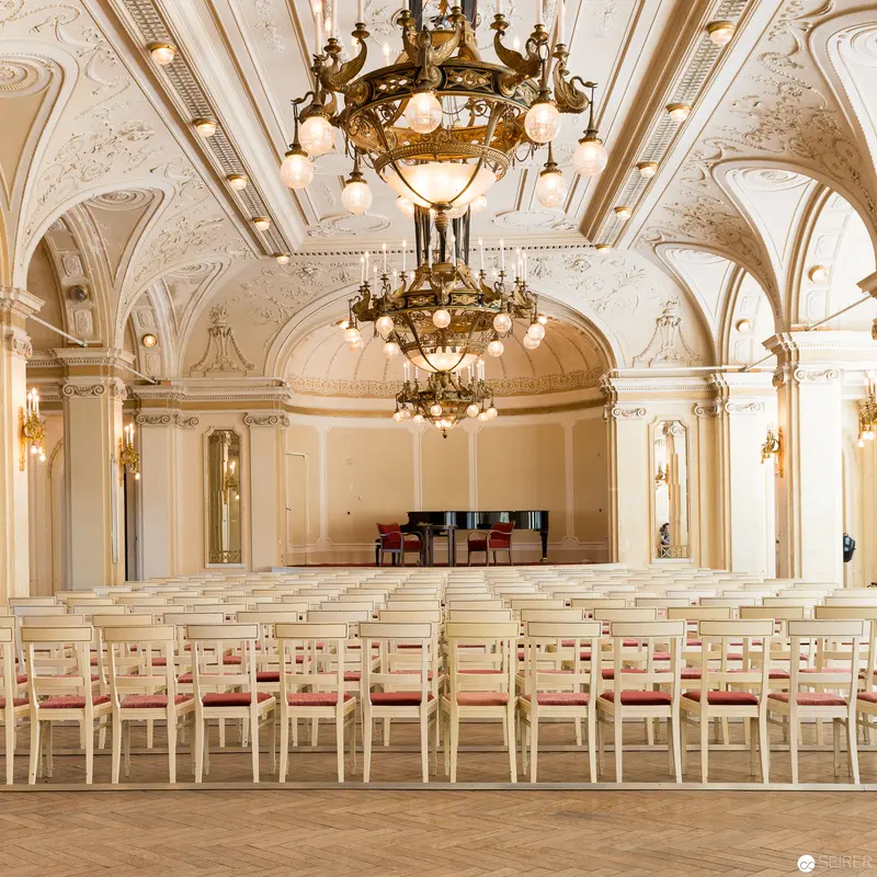 Elegant Concert Hall with Ornate Chandeliers and Pristine White Chairs