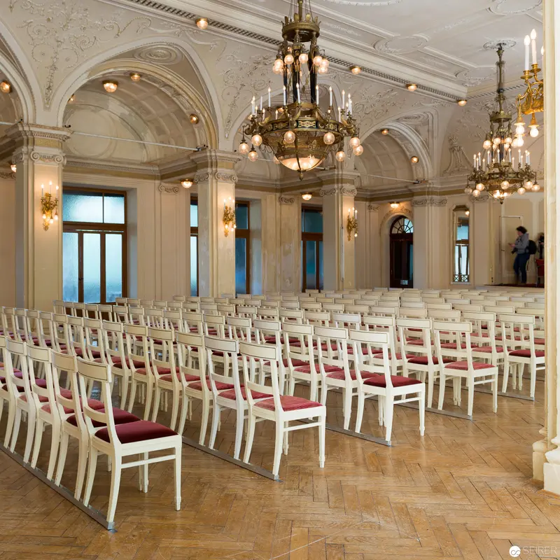 Elegant White and Gold Ballroom with Rows of Chairs and Ornate Chandeliers