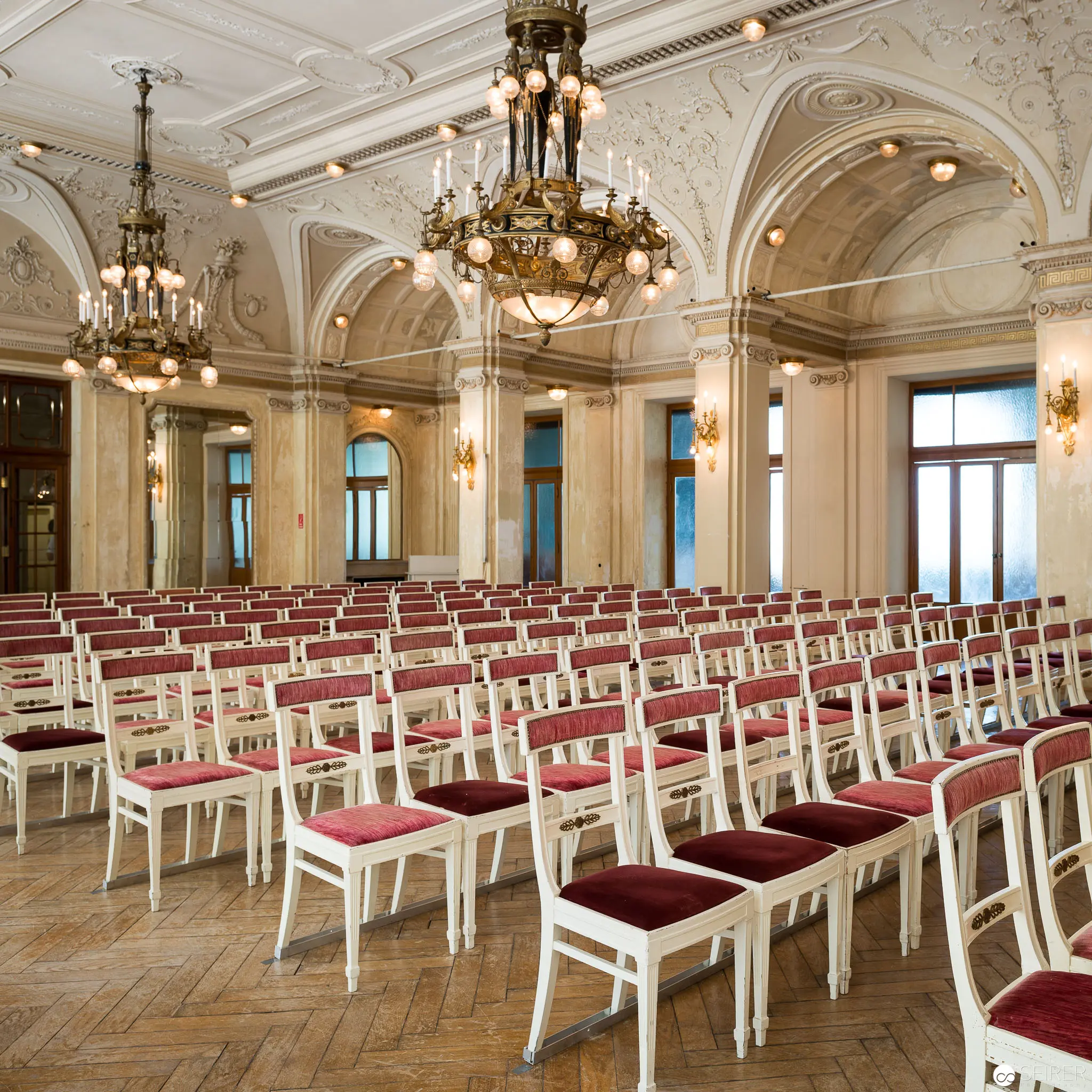 Elegant Neoclassical Hall with Rows of Red-Upholstered Chairs Under Crystal Chandeliers