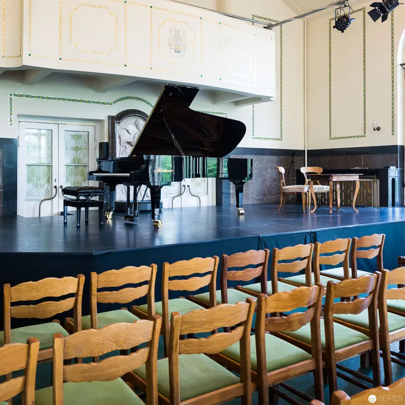 Grand Piano on Elevated Stage with Wooden Chairs in Concert Hall Setting