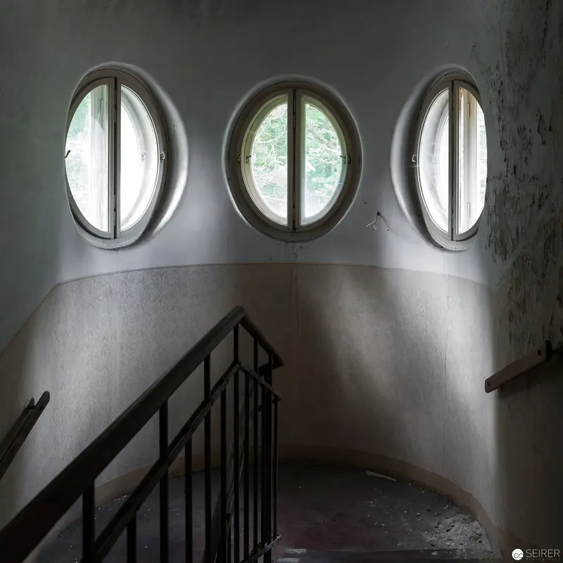 Ghostly Oval Windows Illuminating Abandoned Stairwell Interior