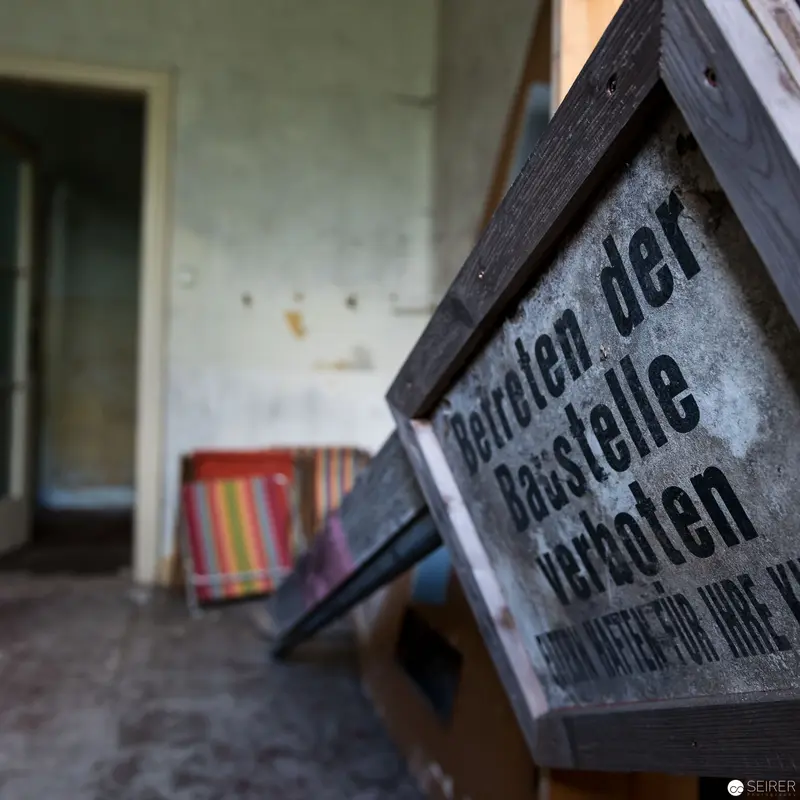 Vintage Wooden Sign in Abandoned Interior with Faded Textiles and Doorway