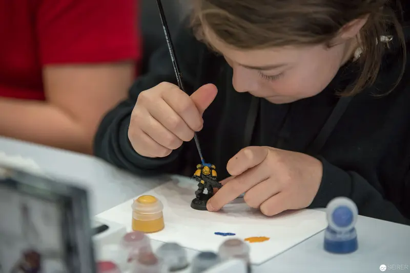 Young Painter Meticulously Detailing Miniature Figure with Precision Brush Technique