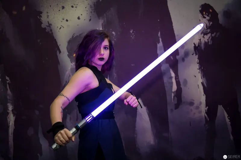 Woman with Purple Hair Wielding Illuminated Lightsaber in Dark Theatrical Setting