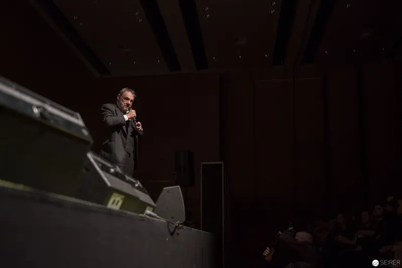Orator Speaks Dramatically on Darkened Stage Under Focused Lighting
