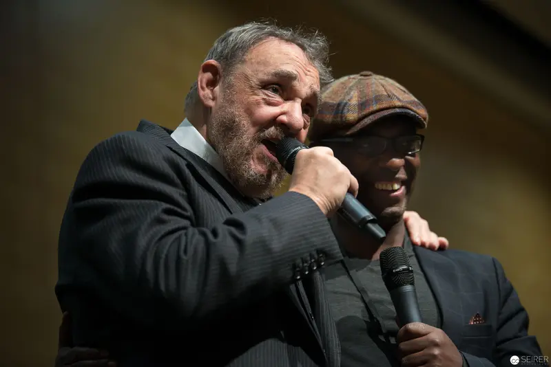 Two Performers Sharing Microphone in Dramatic Stage Performance