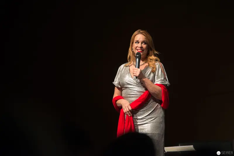 Comedian in Metallic Silver Dress Performing Stand-Up on Dark Stage