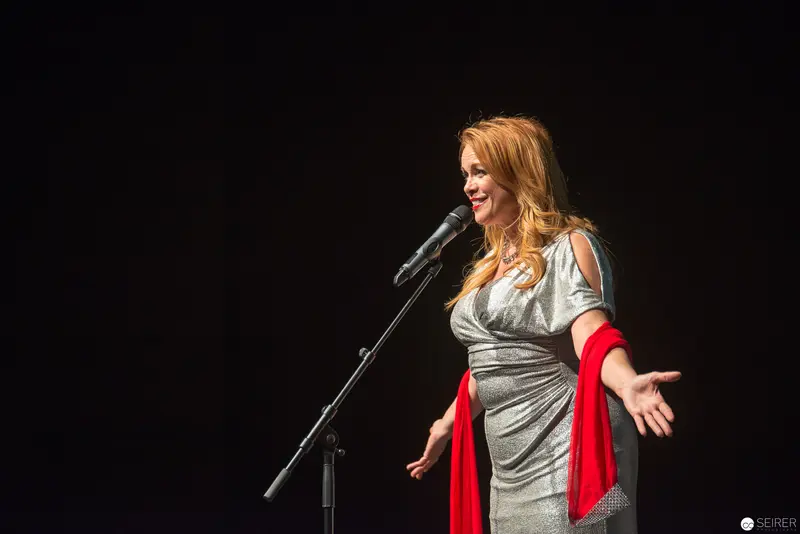 Performer in Silver Dress with Red Shawl on Dark Stage During Theatrical Performance