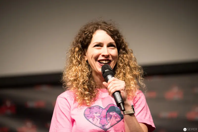 Comedian in Pink Shirt Laughing Onstage with Microphone