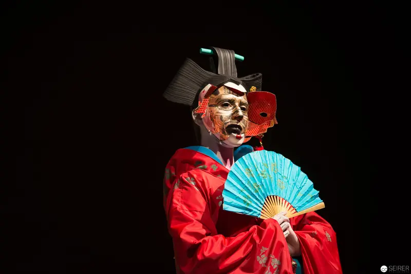 Japanese Kabuki Actor in Red Robe Performing with Blue Fan Against Black Background