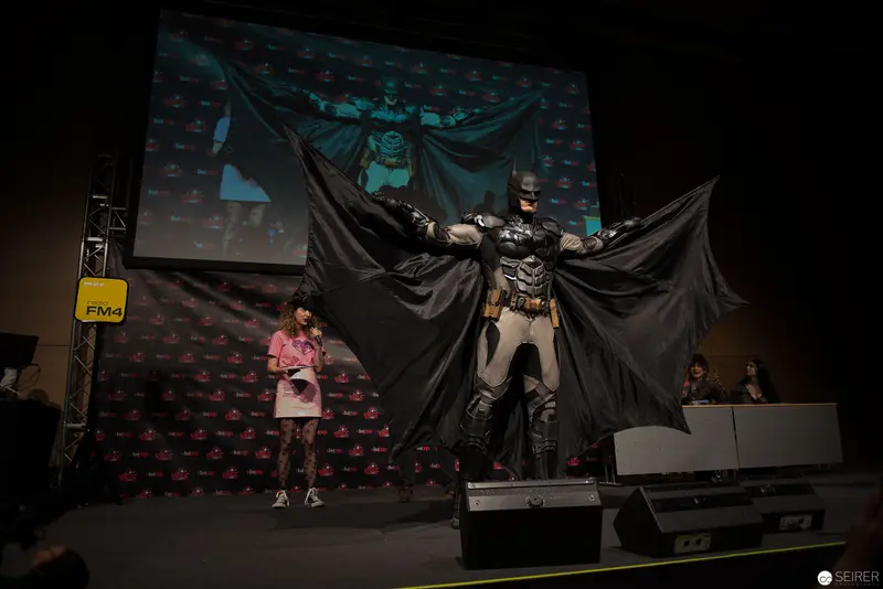 Costumed Batman Performer Poses Dramatically on Convention Stage with Backdrop