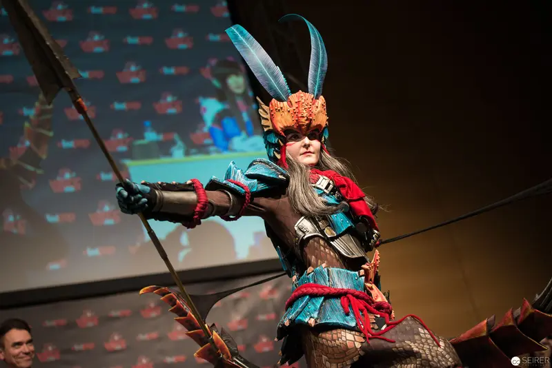 Costumed Performer in Elaborate Winged Headdress Wielding Spear at Stage Event