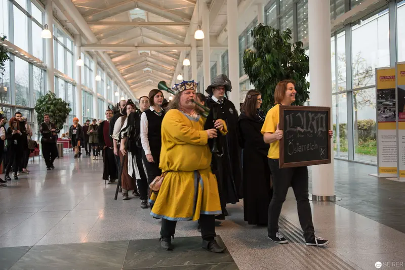 Medieval Reenactors in Contemporary Glass-Walled Corridor Procession