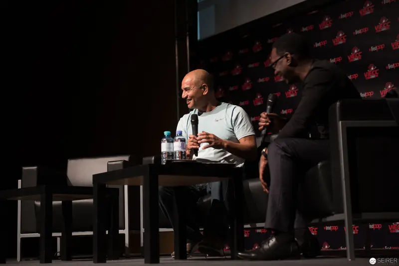 Panel Discussion at Convention with Bald Speaker in White Shirt