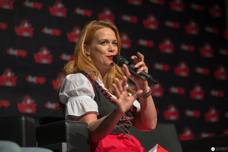 Woman in Traditional Dress Speaks at Event with Red and Black Branding