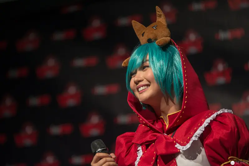 Cosplay Performer in Turquoise Wig and Red Hood at Convention Event