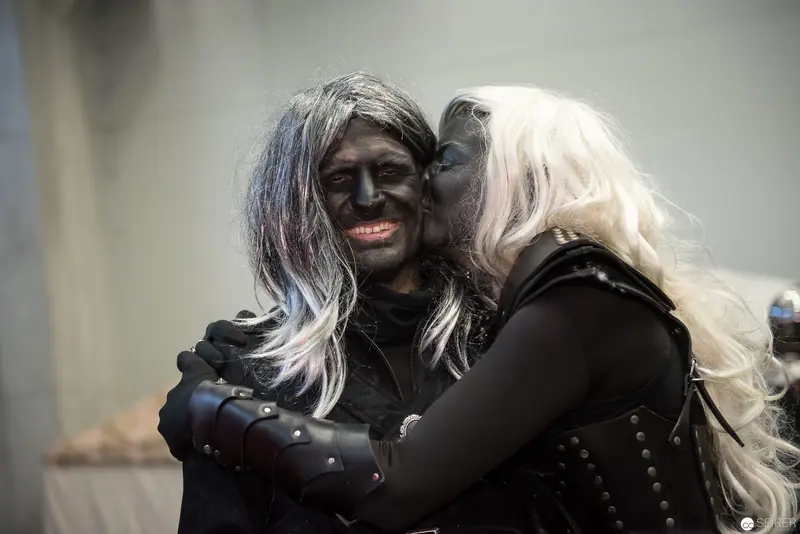 Intimate Embrace of Two Performers in Dark Costumed Attire and Wigs