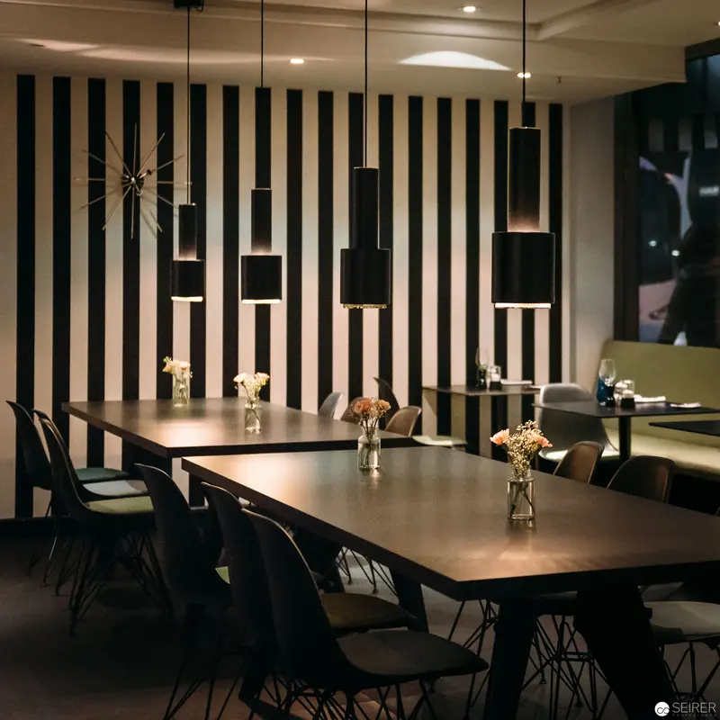 Monochromatic Dining Space with Geometric Pendant Lighting and Striped Accent Wall