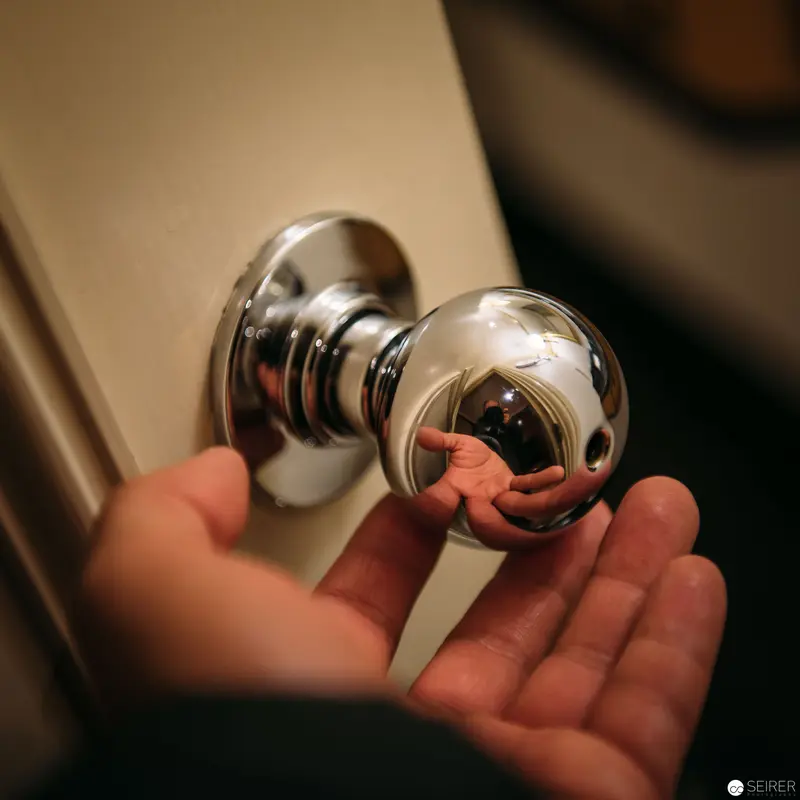 Polished Chrome Doorknob with Reflective Surface and Human Hand