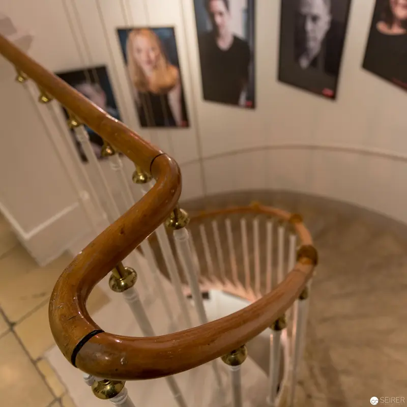 Wooden Handrail Curves Against Photographic Portrait Gallery Wall