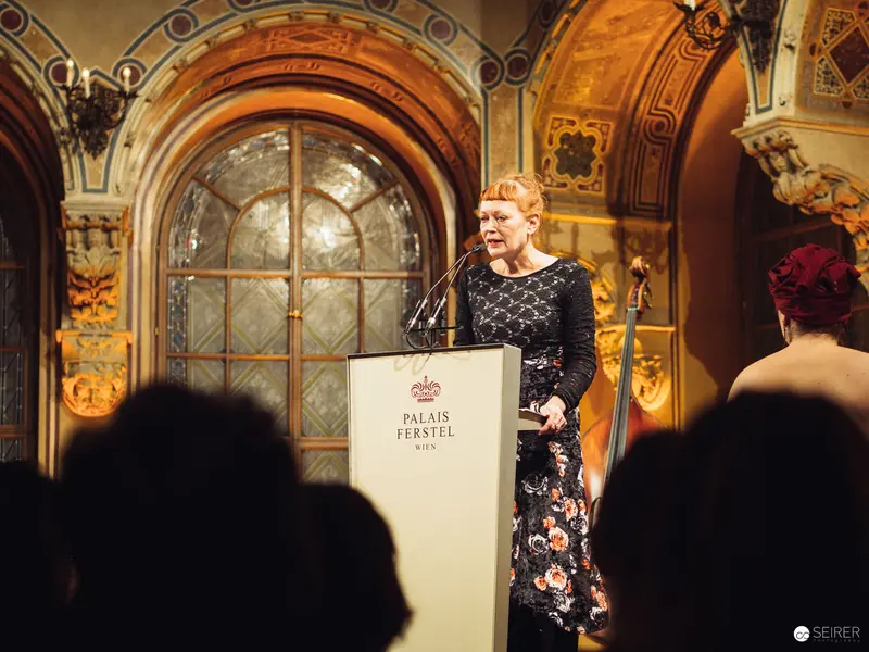 Woman Speaking at Podium in Ornate Palais Ferstel During Formal Event