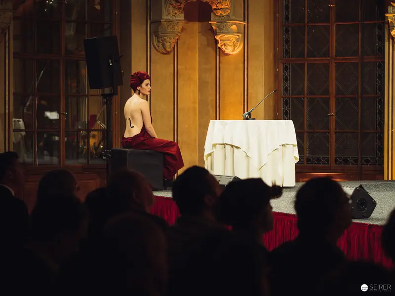 Performer in Red Seated at Staged Table During Performance Event