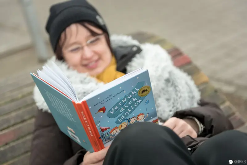 Janett Cernohuby Reading Outdoors in Winter, Absorbed in Blue-Covered Book