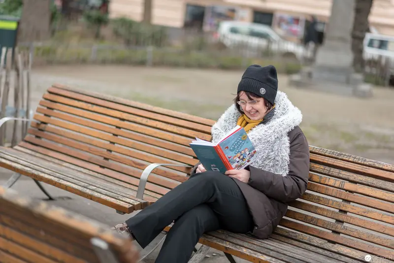 Janett Cernohuby Reading on Wooden Park Bench Near Hauptbücherei Wien