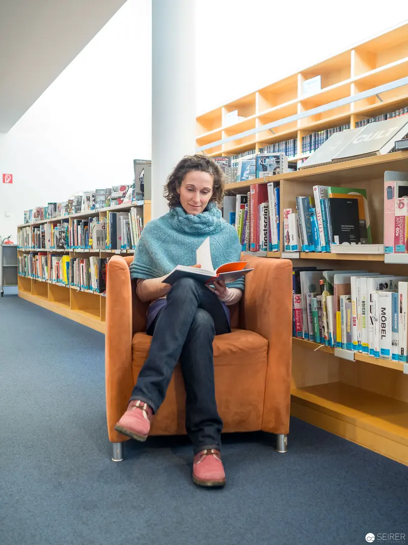Woman Reading in Cozy Library Armchair Surrounded by Bookshelves