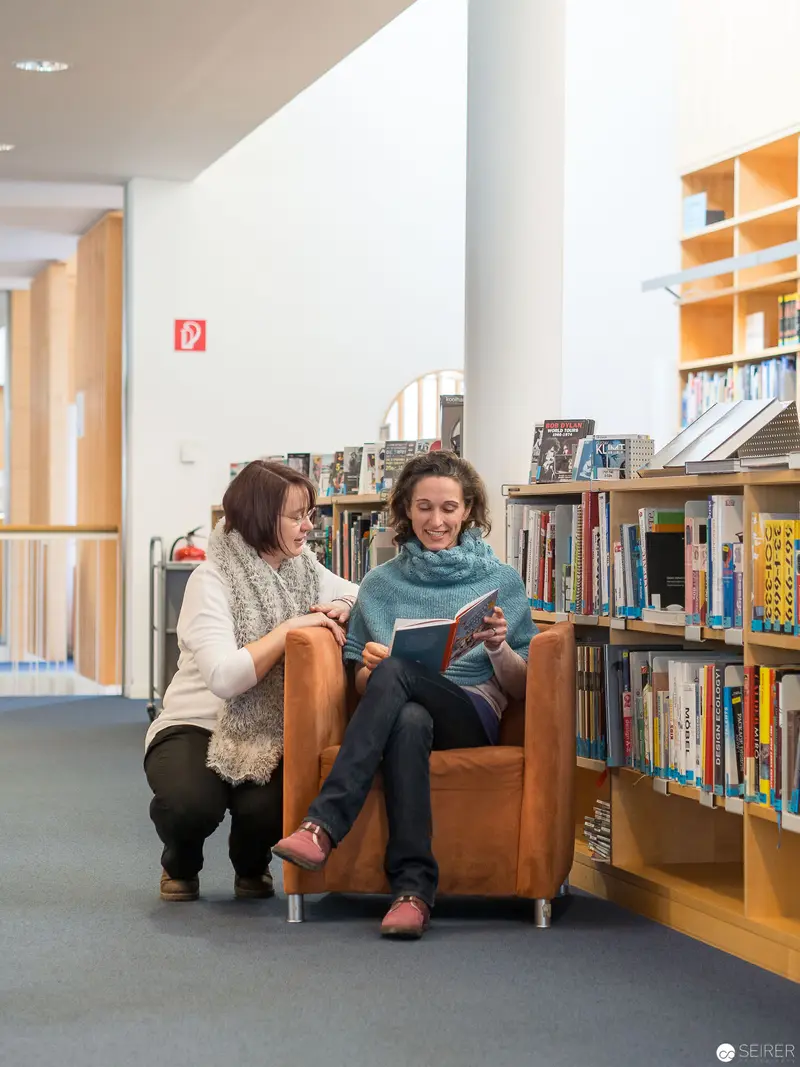 Two Readers in Intimate Library Space, Seated Near Bookshelves
