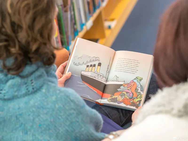 Children Reading Illustrated Book About Titanic Ship in Library Setting