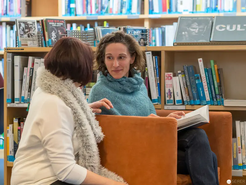 Two Women Conversing in Library Surrounded by Bookshelves