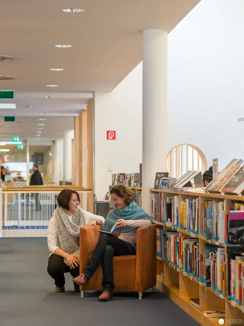 Two Women Engaged in Conversation amid Library Bookshelves